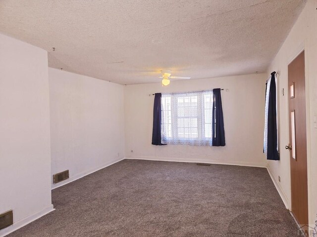 empty room with visible vents, dark carpet, a textured ceiling, and baseboards