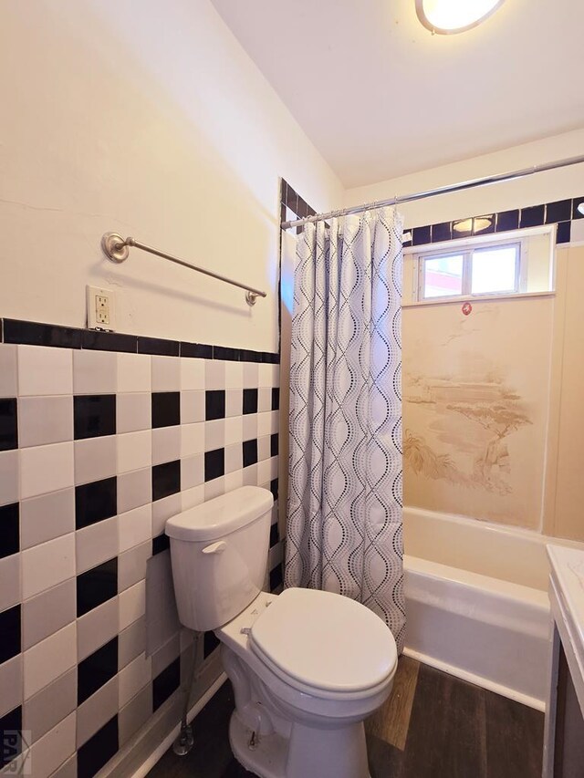 bathroom with toilet, wood finished floors, tile walls, wainscoting, and shower / bath combination with curtain