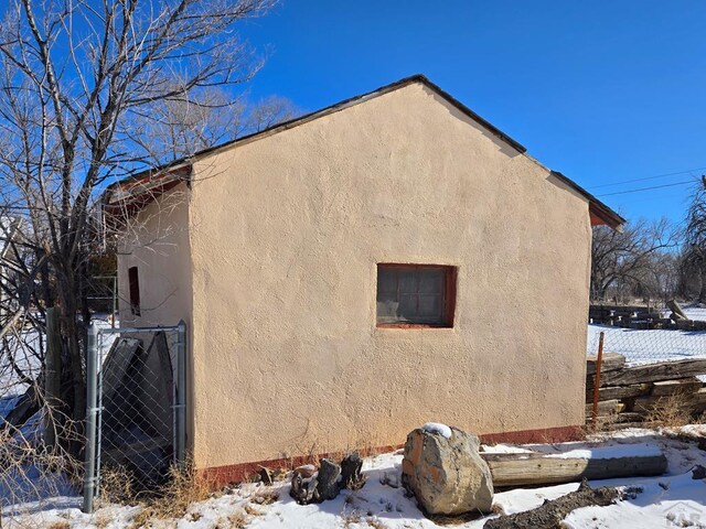 snow covered property with fence and stucco siding