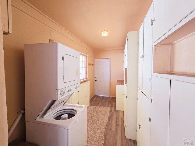 laundry area featuring laundry area, stacked washer / dryer, light wood-type flooring, and crown molding