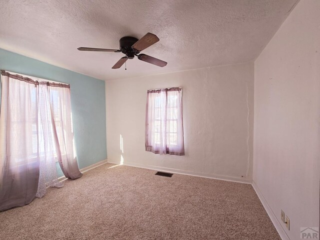 unfurnished room featuring a textured ceiling, carpet flooring, visible vents, baseboards, and a ceiling fan