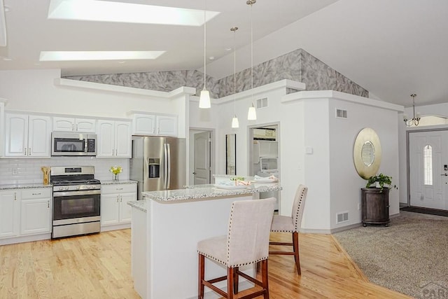 2221 Cliffmoor Ln, Pueblo, CO 81008 - kitchen featuring appliances with stainless steel finishes, high vaulted ceiling, a kitchen breakfast bar, white cabinets, and light wood-style floors