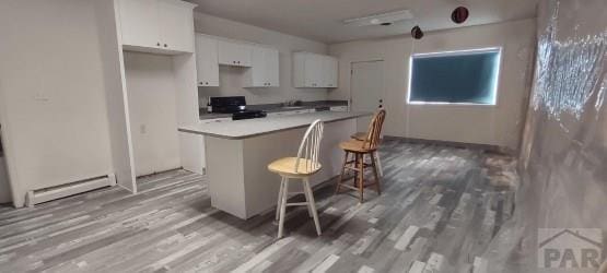 kitchen featuring white cabinets, a baseboard radiator, a breakfast bar area, light countertops, and range with electric stovetop