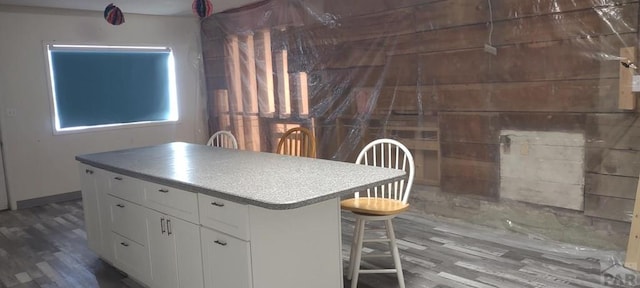 kitchen with dark wood-type flooring, a breakfast bar area, white cabinetry, and a center island