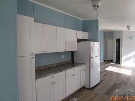 326 Katherine St, Avondale, CO 81022 - kitchen featuring white cabinetry, freestanding refrigerator, dark stone countertops, and wood finished floors