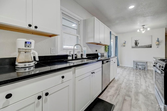 kitchen featuring stainless steel appliances, light wood-style flooring, white cabinets, a sink, and a textured ceiling