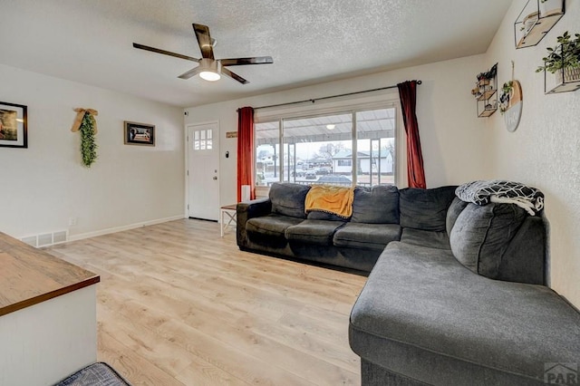 living room featuring a textured ceiling, ceiling fan, visible vents, baseboards, and light wood-type flooring