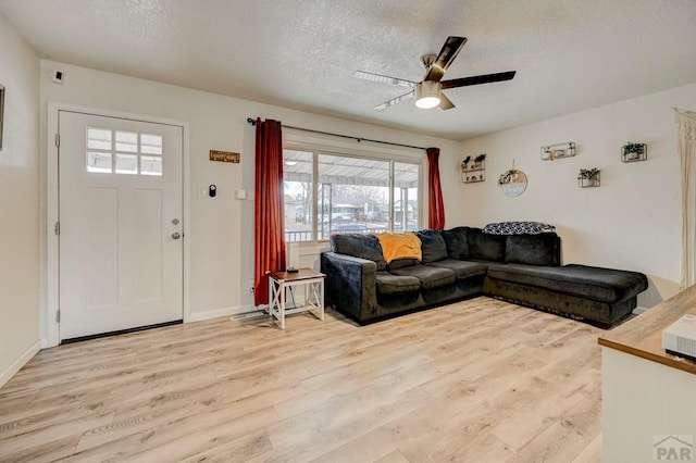 living room with light wood-type flooring, ceiling fan, a textured ceiling, and baseboards