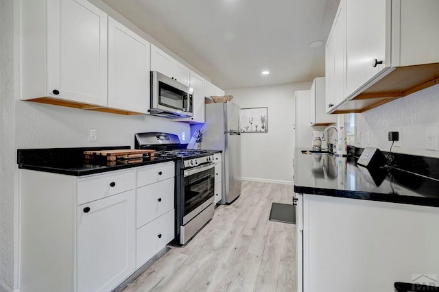 kitchen with stainless steel appliances, dark countertops, light wood-style floors, white cabinets, and a sink