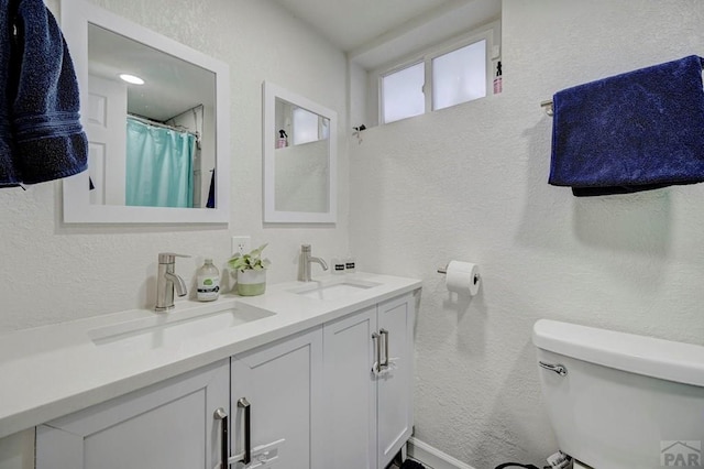 bathroom featuring toilet, double vanity, a sink, and a textured wall