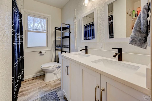 bathroom with double vanity, wood finished floors, a sink, and toilet