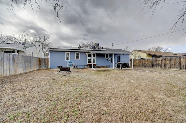 rear view of house with entry steps, a fenced backyard, and roof mounted solar panels