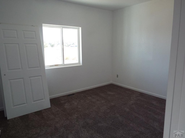 unfurnished room with dark carpet and baseboards