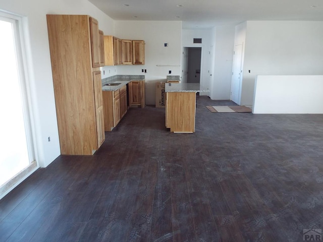 kitchen featuring light stone countertops, open floor plan, dark wood-style flooring, and a center island