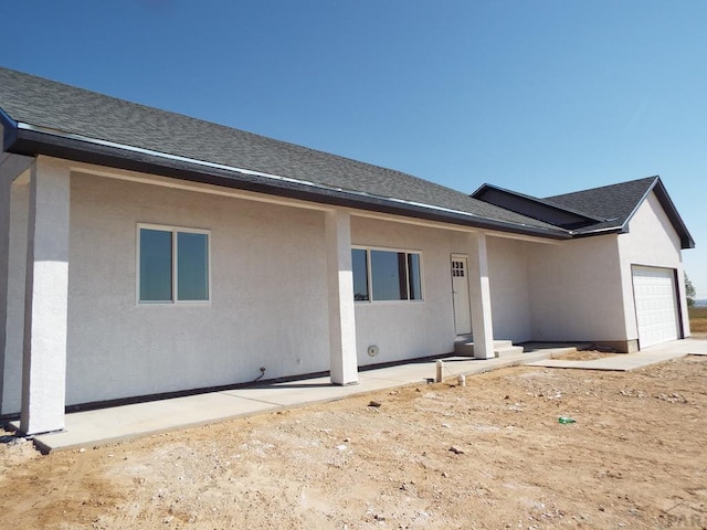 rear view of house featuring an attached garage, a shingled roof, and stucco siding