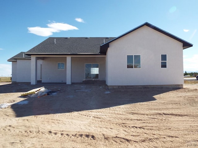 rear view of property with a shingled roof and stucco siding