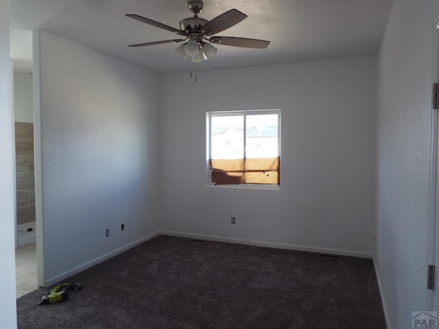 spare room featuring baseboards, dark carpet, and a ceiling fan