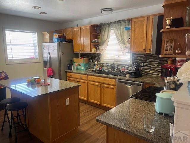 kitchen featuring a center island, dark wood-style flooring, open shelves, stainless steel appliances, and a sink