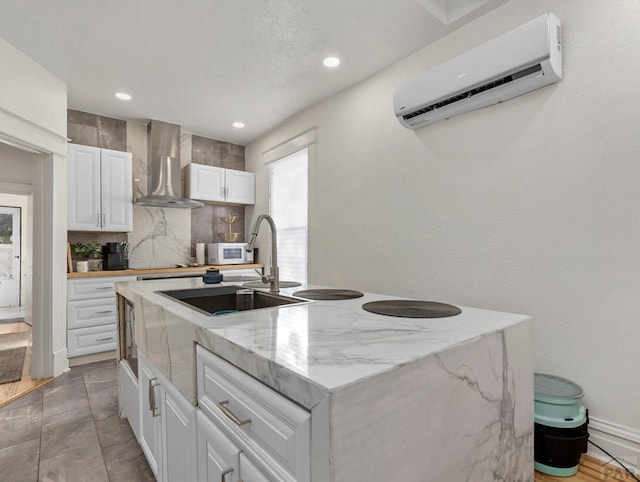 kitchen featuring white microwave, white cabinets, an AC wall unit, wall chimney range hood, and an island with sink