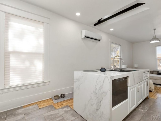 kitchen featuring a wall unit AC, a kitchen island with sink, a sink, white cabinets, and pendant lighting