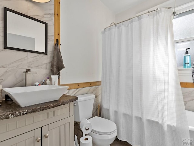 full bathroom featuring toilet, shower / bathtub combination with curtain, tile walls, and vanity