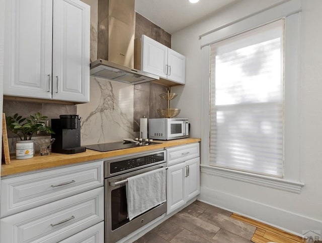 kitchen with wall chimney exhaust hood, wood counters, stainless steel oven, and white cabinetry