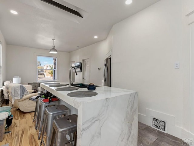 kitchen featuring visible vents, a kitchen island with sink, light wood-type flooring, stainless steel fridge, and a kitchen bar