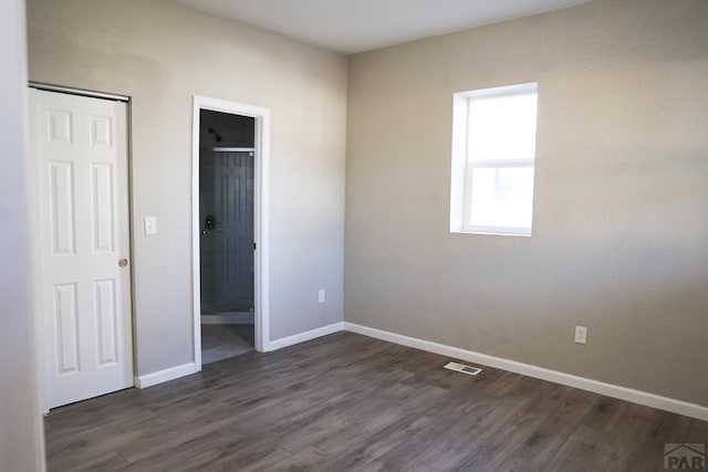 unfurnished bedroom featuring dark wood-type flooring, visible vents, connected bathroom, and baseboards