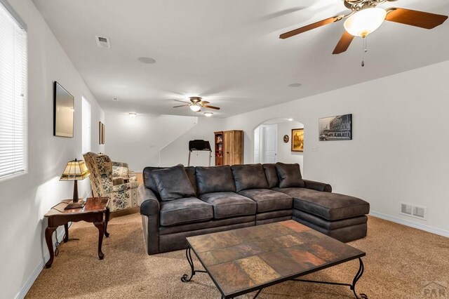 living room featuring arched walkways, baseboards, visible vents, and light colored carpet