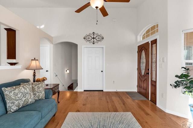 entrance foyer featuring arched walkways, high vaulted ceiling, light wood finished floors, and baseboards