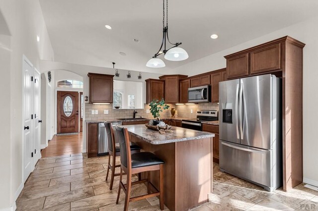 kitchen featuring a center island, stainless steel appliances, hanging light fixtures, decorative backsplash, and a sink