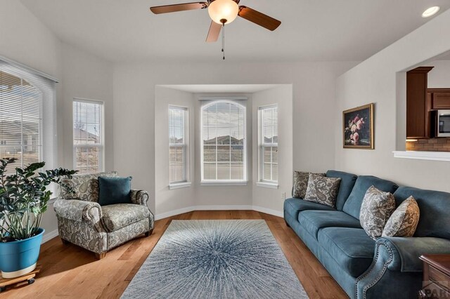 living room featuring light wood-style flooring, baseboards, and a ceiling fan