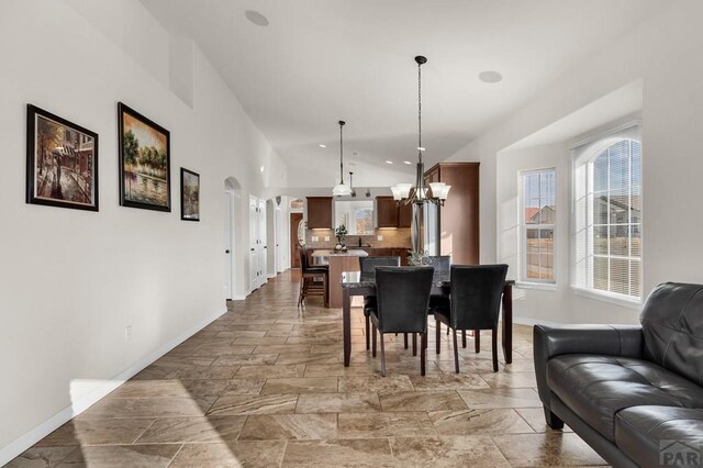 dining area featuring arched walkways, vaulted ceiling, a notable chandelier, and baseboards