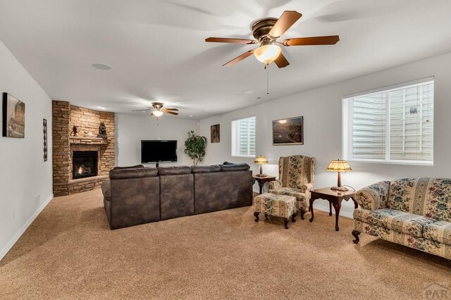 carpeted living room with a ceiling fan, a stone fireplace, and baseboards