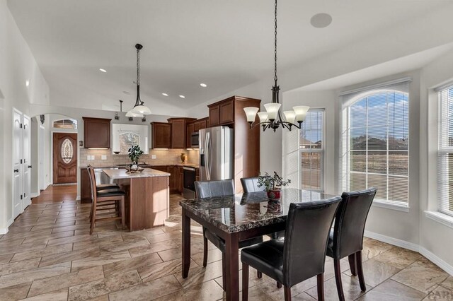 dining room featuring a wealth of natural light, arched walkways, a chandelier, and vaulted ceiling