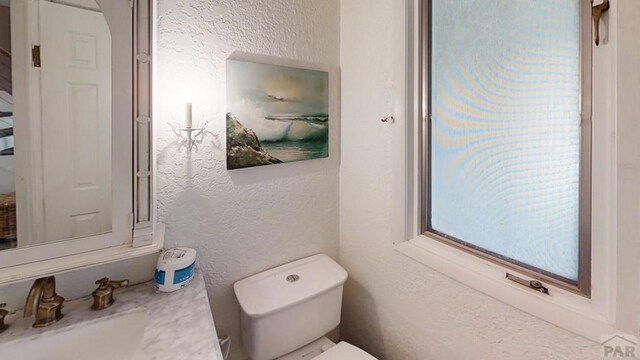 half bath with toilet, vanity, and a textured wall