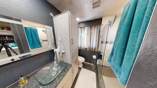 bathroom featuring a stall shower, visible vents, a textured wall, toilet, and vanity