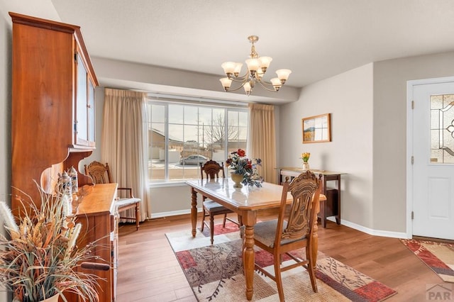 dining room featuring light wood-style floors, a notable chandelier, and baseboards