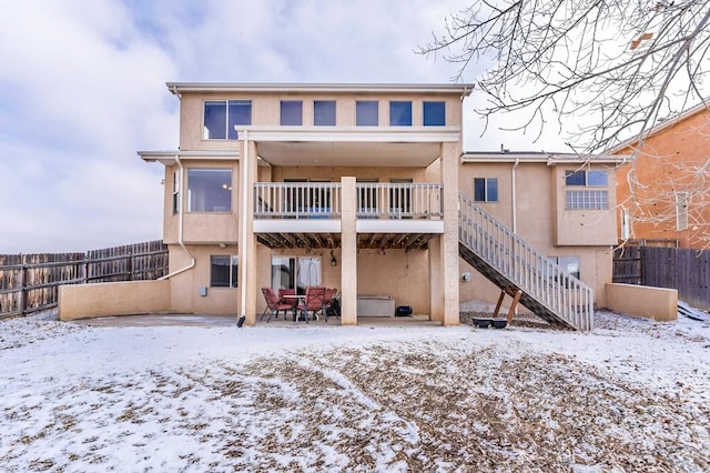 snow covered house featuring a patio area, stairway, fence, and stucco siding