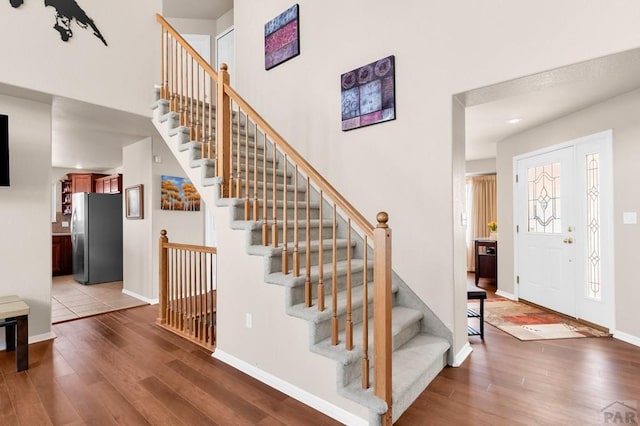 staircase featuring wood finished floors, a towering ceiling, and baseboards