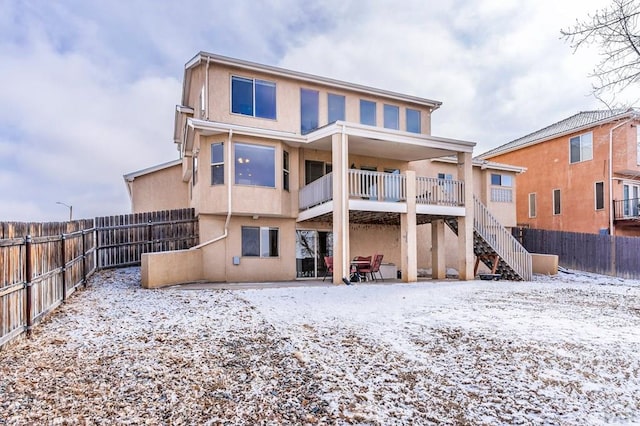 snow covered rear of property with a fenced backyard, stairs, and stucco siding