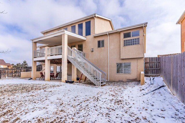 snow covered rear of property featuring a patio area, a fenced backyard, stairway, and stucco siding