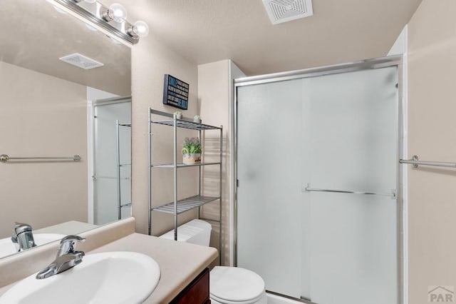 bathroom with a stall shower, visible vents, vanity, and toilet