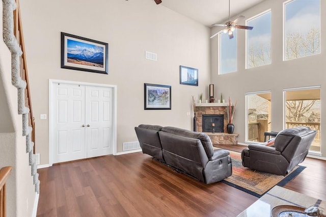 living room featuring dark wood-style floors, visible vents, a ceiling fan, and a stone fireplace