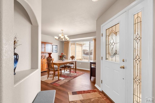 entryway featuring baseboards, a textured ceiling, wood finished floors, and an inviting chandelier