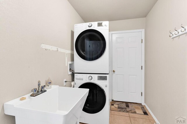 washroom featuring tile patterned flooring, laundry area, a sink, baseboards, and stacked washer and clothes dryer