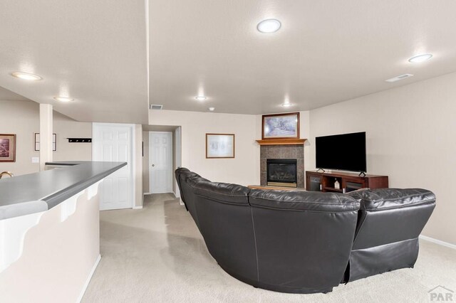 living area featuring light carpet, a tiled fireplace, visible vents, and baseboards