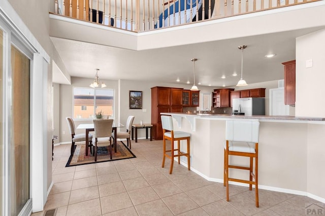 kitchen featuring brown cabinetry, glass insert cabinets, a breakfast bar, light countertops, and stainless steel refrigerator with ice dispenser