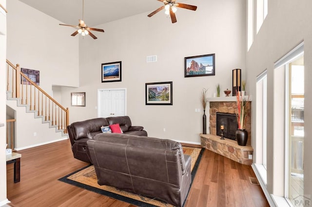 living area with a fireplace, wood finished floors, visible vents, baseboards, and stairway