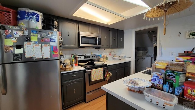 kitchen with light countertops, appliances with stainless steel finishes, washer and clothes dryer, and light wood-style floors